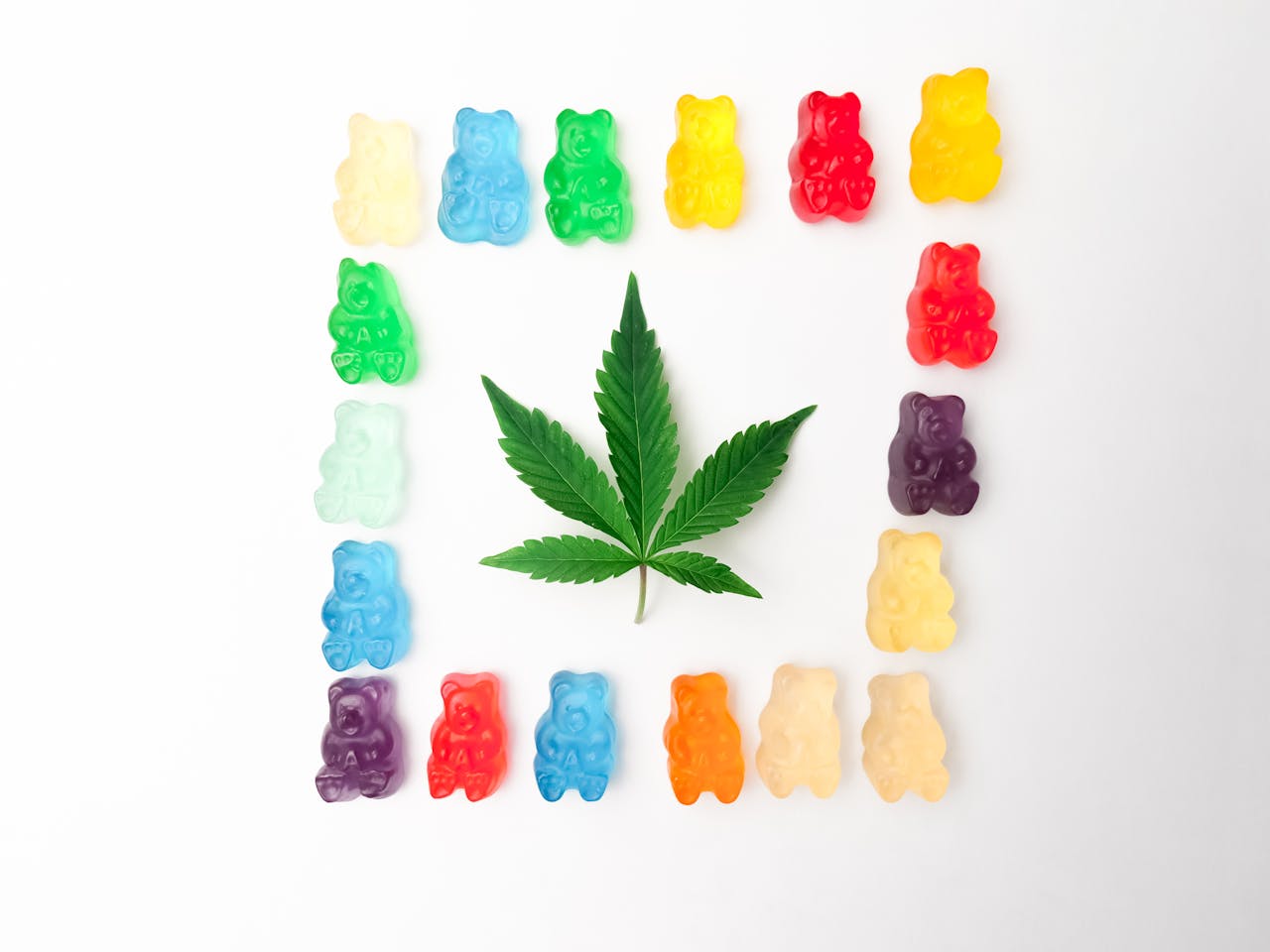 services-02 Vibrant gummy bears form a colorful border around a cannabis leaf on a white background, showcasing edible cannabis culture.